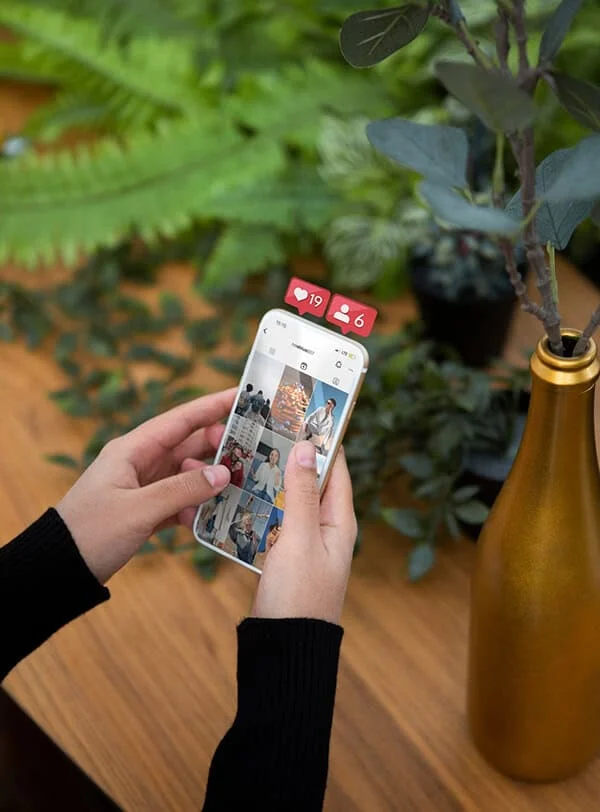 marketing-en–redes-sociales-eduweb-barcelona Foto de una persona usando un teléfono móvil con notificaciones en redes sociales, en un entorno natural con plantas verdes y una decoración moderna diseñando una web en Barcelona.